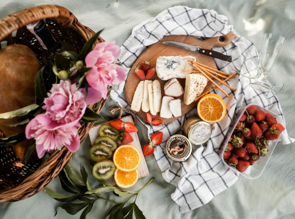 A colourful picnic spread with flowers, fruits and cheeses.